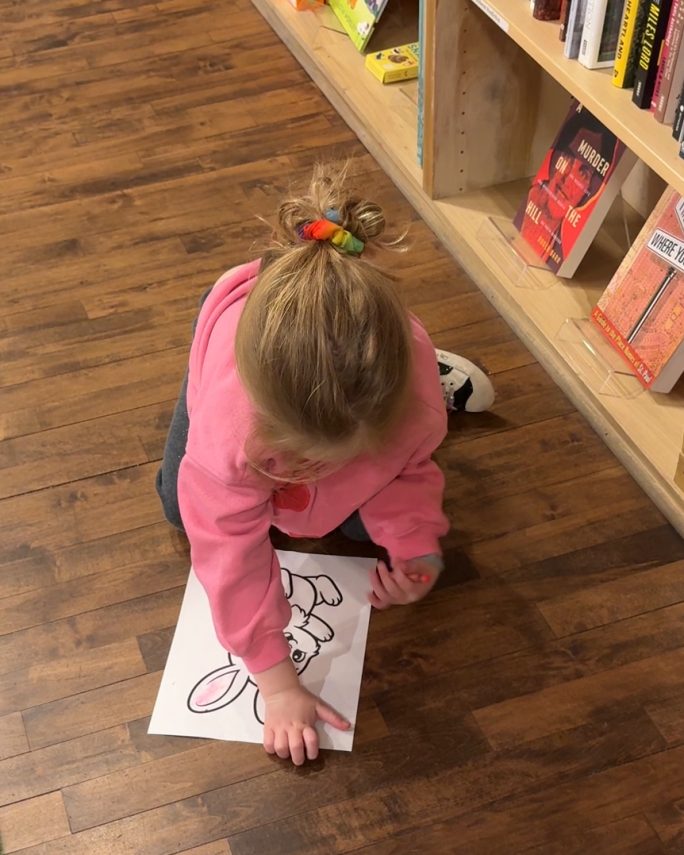 A little girl is sitting on the floor, coloring a picture of a rabbit